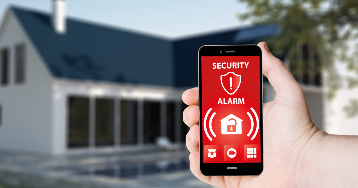Une main tient un téléphone avec une application d'alarme de sécurité sur un écran sur le fond d'une maison. Tous les graphiques de l'écran ont été créés.